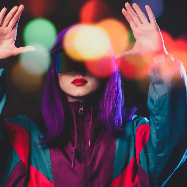 Frau mit lila Haaren und breiter verspiegelter Visierbrille in einer Retro-Trainingsjacke, beide Hände offen erhoben, dahinter bunte unscharfe Lichtpunkte.
